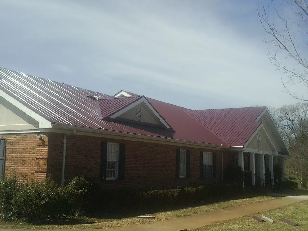 Red metal roof with gabled entries on a long brick building, from a Hail Damage Roof Repair job in Charlotte