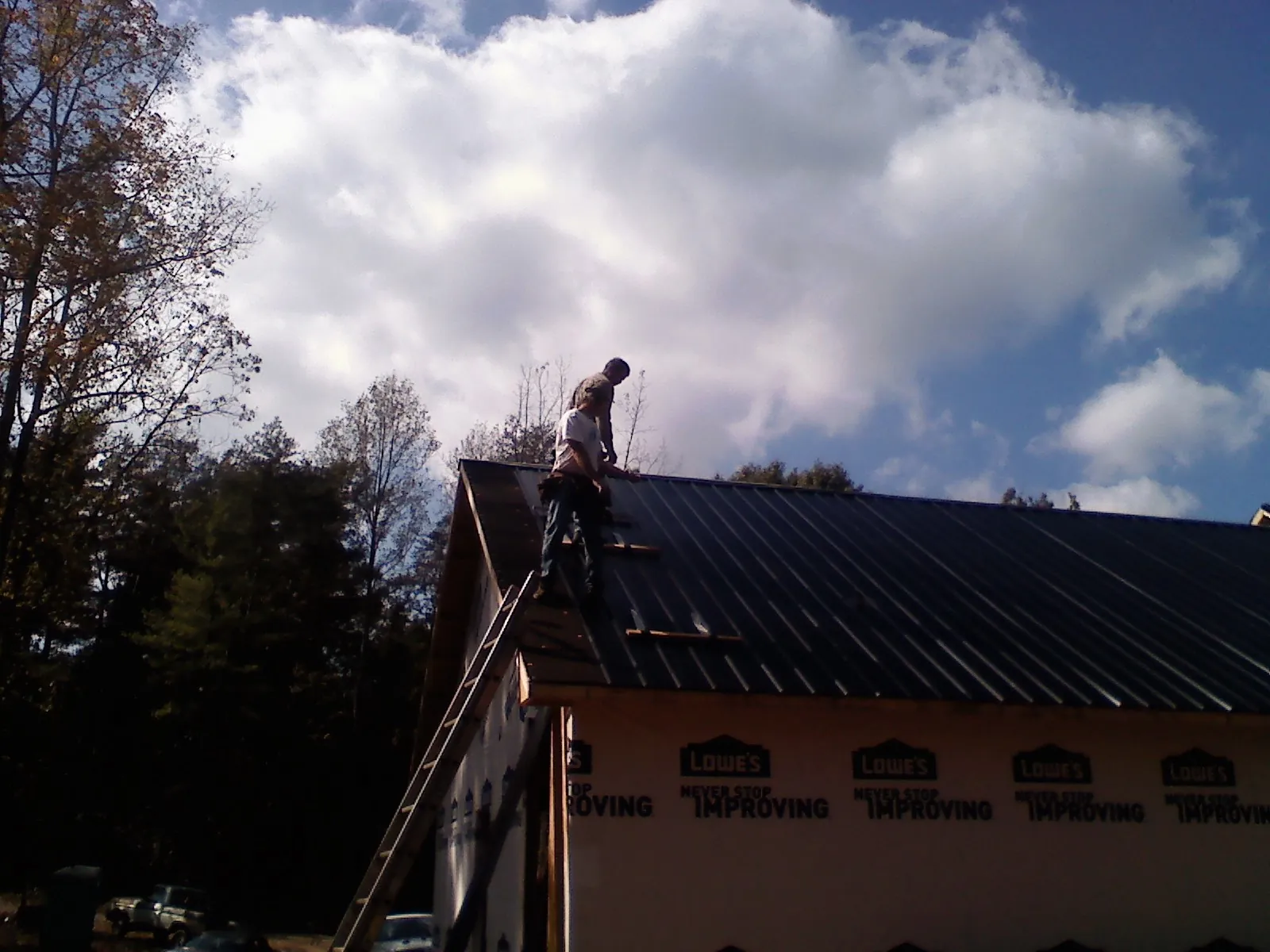 Roofer fastening dark metal panels high against a cloudy sky, from a Roof Inspection job in Charlotte